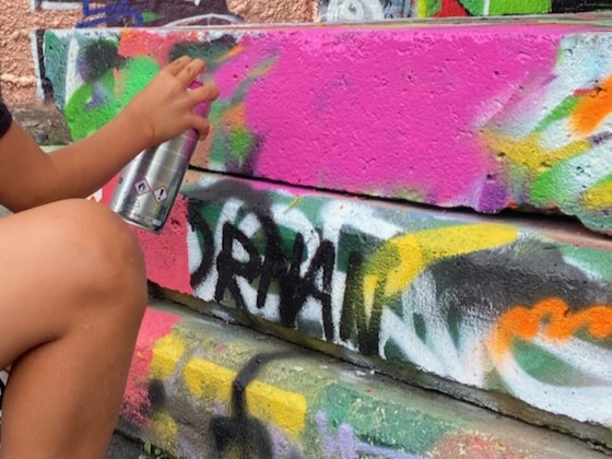 Hand på sprayburk framför en vägg full med klotter