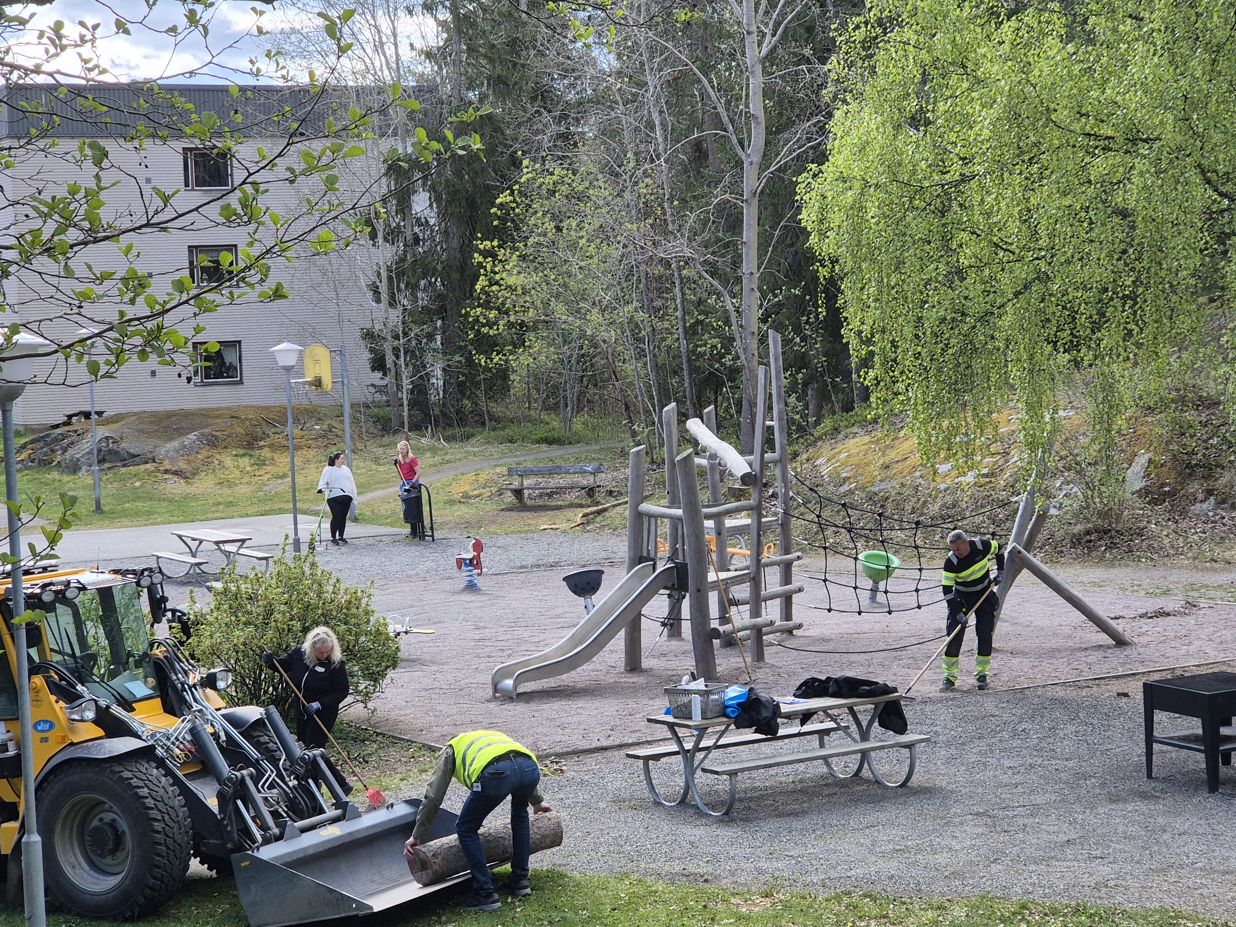 Personal från VärmdöBostäder som gör iordning en lekplats. Rensar ogräs och skräp.