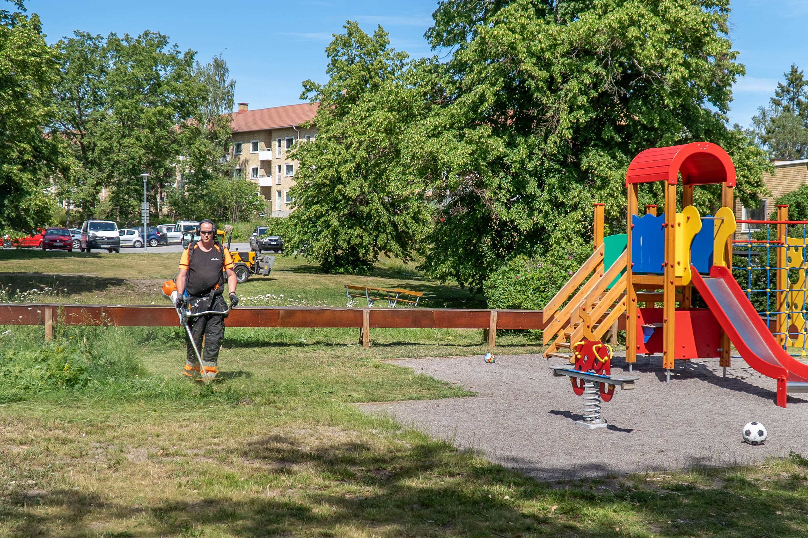 Man som trimmar gräs vid en lekplats